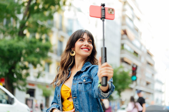 Young woman vlogging with selfie stick and smartphone in the city