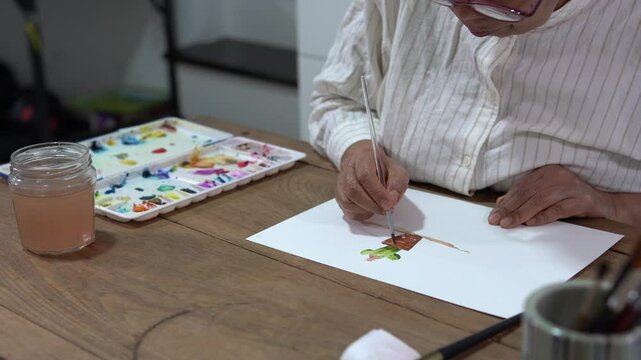 Senior woman painting a watercolor cactus and pot at home in peaceful atmosphere  