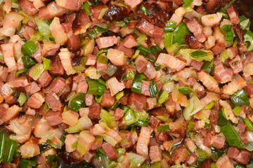 A detailed overhead close-up shows diced pancetta and chopped green onions cooking in a pan, with a slight sheen of oil