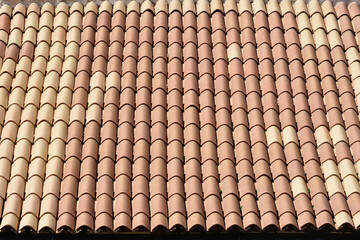 A close-up of a roof covered with rows of red and beige barrel tiles