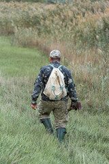 Mature hunter man holding a shotgun and walking through a field