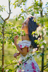 portrait of a beautiful woman in a dress in a blooming apple orchard enjoying a sunny spring day