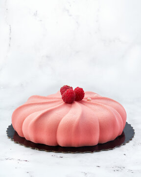 Elegant raspberry and white chocolate mousse cake with velvet texture and fresh raspberries. Side view on white marble with copy space. Perfect for branding, packaging or editorial use.