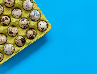Сomplete container box of farm fresh quail eggs on the blue background. Top view.