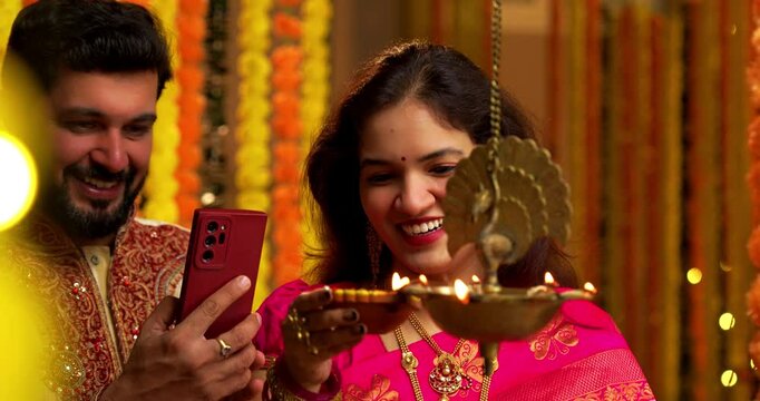 Husband Filming Samai Lighting During Diwali, Indian Married Couple in Saree and Kurta Celebrate Festival by Lighting Traditional Brass Lamp at Night While Smiling and Capturing Moment on Smartphone