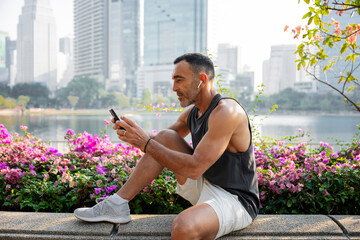 Mature man using smartphone while resting after exercising outdoors in Bangkok