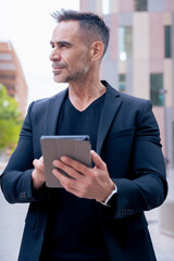Confident businessman standing outdoors using a tablet in a modern urban setting.He appears focused and professional. Concept of digital work, technology, and contemporary business lifestyle. Vertical