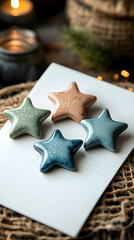Four ceramic star ornaments in muted earth tones, adorned with gold speckles, rest on a white card