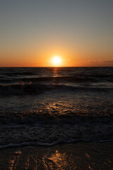 A breathtaking ocean sunset with the sun dipping below the horizon, casting a warm golden glow on the rippling blue water. Serene and picturesque coastal scene.
