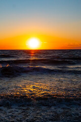 A breathtaking ocean sunset with the sun dipping below the horizon, casting a warm golden glow on the rippling blue water. Serene and picturesque coastal scene.
