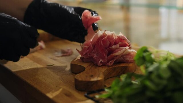 Close-up of slicing and serving meat delicacies on a wooden board. Thin slices of prosciutto, chorizo, lomo, handmade fennel sausage. An exquisite selection of delicious appetizers. Meat plate.