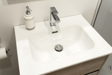 Fototapeta premium Modern bathroom sink with a minimalist rectangular basin and sleek chrome faucet, complemented by a stylish soap dispenser. 