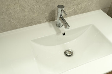 Modern white ceramic bathroom sink with wooden vanity cabinet and chrome faucet. Contemporary and clean design in a tiled bathroom setting.