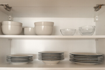 Kitchen cupboard with different clean dinnerware. Shelving with dishes, glasses and cups.