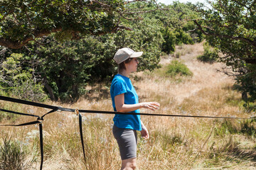 A female slackliner performs acrobatic poses and splits on a slackline stretched between trees on a...
