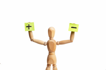 A wooden mannequin toy holding sticky paper with minus and plus signs in his hand on white background