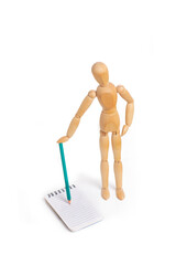 A wooden mannequin toy holding a pencil on a spiral notebook on white background with copy space