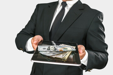 A businessman holds a tablet with American dollars on a light background.