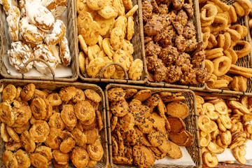 A vibrant assortment of cookies and pastries arranged in wicker baskets, featuring various textures, toppings, and shapes. The display includes iced pastries, nut-topped cookies, chocolate chip treats