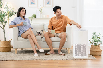 Asian Young couple sitting on sofa with coffee mugs relaxing in their living room with pug dog. One...