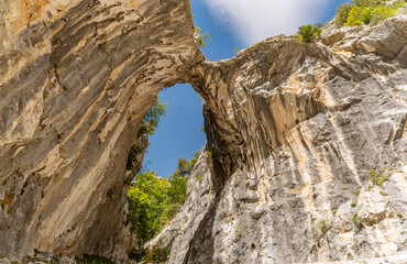 LA GARGANTA DIVINA . Natural rock arch formation in the Picos de Europa mountains, Spain, viewed from below against a bright blue sky.