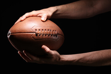 Close-up of an athlete's hand playing American football, holding a football in the air on a black background