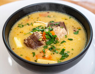 A steaming bowl of Sopa de Pata, a traditional Salvadoran soup, garnished with herbs and vegetables, showcasing a comforting local dish.