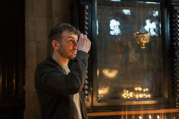 Modern Orthodox Christian man praying and lighting candles in a monumental Georgian church. A...