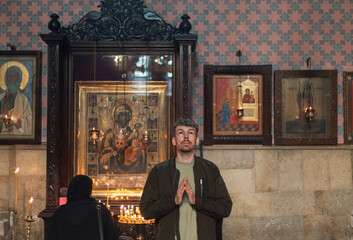 Modern Orthodox Christian man praying and lighting candles in a monumental Georgian church. A...