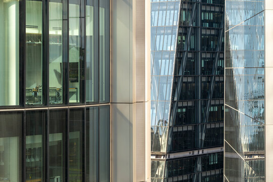 Close-up of illuminated glass offices with grid reflections and modern towers in background, ideal for corporate, finance and commercial urban visuals.