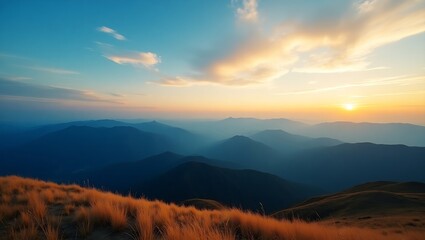Fototapeta premium Panoramic view of majestic mountain range under a vibrant sunrise sky, golden grassy hills in foreground, misty peaks fading into tranquil natural beauty.