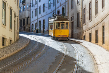 Historic yellow tram climbs a steep cobbled street in Lisbon, Portugal, surrounded by old buildings...