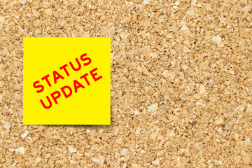 Yellow note paper with word status update on cork board background with copy space