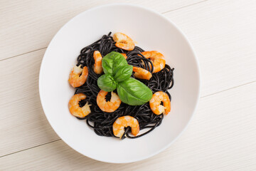 Pasta with cuttlefish ink, shrimp, basil in a white bowl on wooden table. Mediterranean cuisine. Top view.