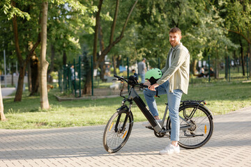 Man enjoys biking in a park on a sunny day while wearing a helmet and smiling at the camera