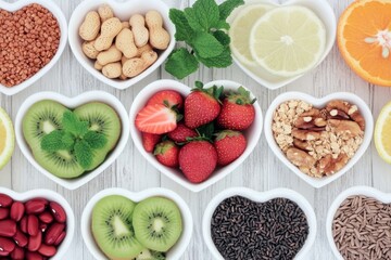 Healthy heart-shaped food bowls on white wooden surface, displaying various fruits, nuts, seeds, and grains, promoting healthy eating