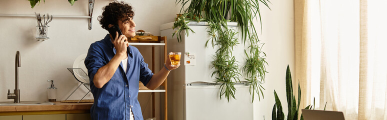 Stylish young man enjoying a drink while chatting on the phone in a cozy kitchen