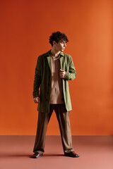 Fashionable young man showcasing stylish outfit against vibrant orange backdrop
