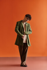 Fototapeta premium Stylish man in a green coat poses against a vibrant orange backdrop in contemporary setting
