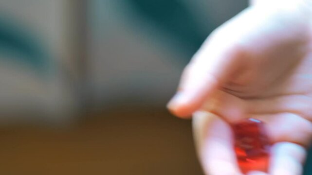 A close-up shot of a child's hand holding a bright red gummy jelly marmalade candy, focusing on its texture and color.