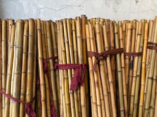 Bundles of Bamboo Sticks Tied with Red Fabric – Traditional Natural Material for Construction, Crafts, or Decoration, Displayed at a Local Market or Store in Indonesia