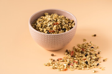 Side view of a ceramic bowl with granola on the light orange background . Muesli with dried fruit close-up .
