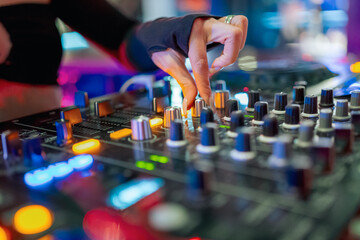 A DJ's hand adjusting knobs on a professional audio mixer in a vibrant club setting, highlighting the dynamic and engaging atmosphere of live music mixing.