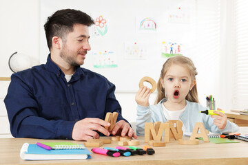 Little girl learning letters with teacher at desk indoors