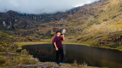 joven turista atractivo en América Latina, feliz mientras usa un teléfono inteligente mirada a un espacio publicidad y aislada en un fondo un lago naturaleza,contactar,celular,quechua