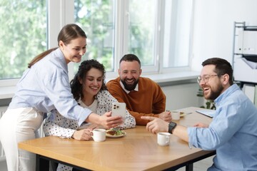 Woman showing her colleagues something on smartphone during lunch break in office