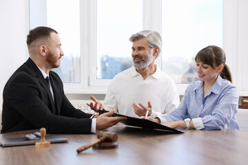 Clients signing notarial paperwork during meeting with lawyer at wooden desk indoors