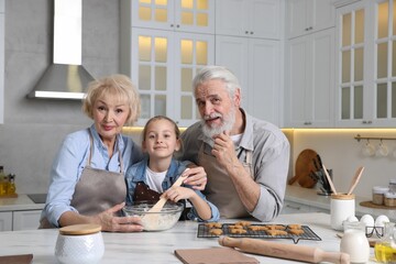 Grandparents and their granddaughter cooking together at white marble table in kitchen