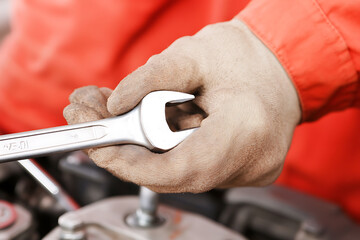 Obraz premium Gloved hand grips a wrench, ready for automotive repair. The mechanic's tool is poised above the engine, symbolizing precision and expertise.