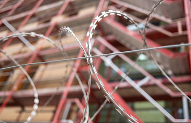 Nahaufnahme von Stacheldrahtzaun vor moderner Geb&auml;udefassade &ndash; Sicherheitskonzept in urbaner Umgebung
